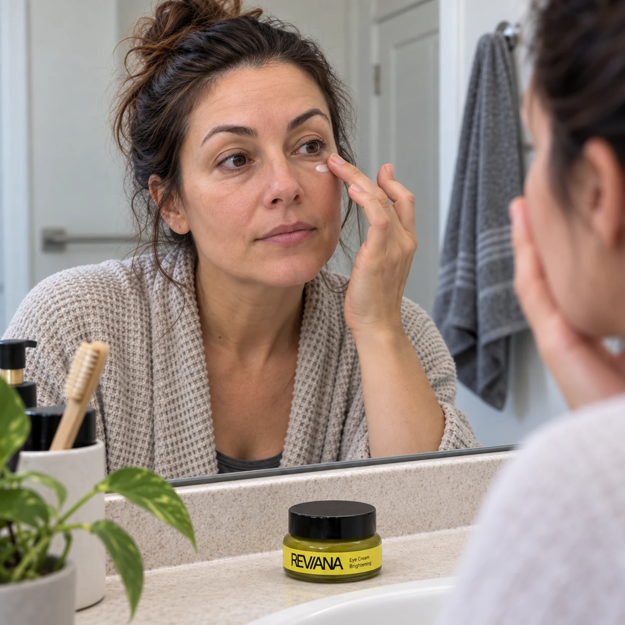 Woman gently applying Reviana Eye Cream while looking in a bathroom mirror