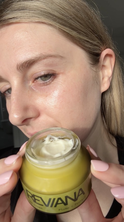 A customer holding the open day cream jar beside her face