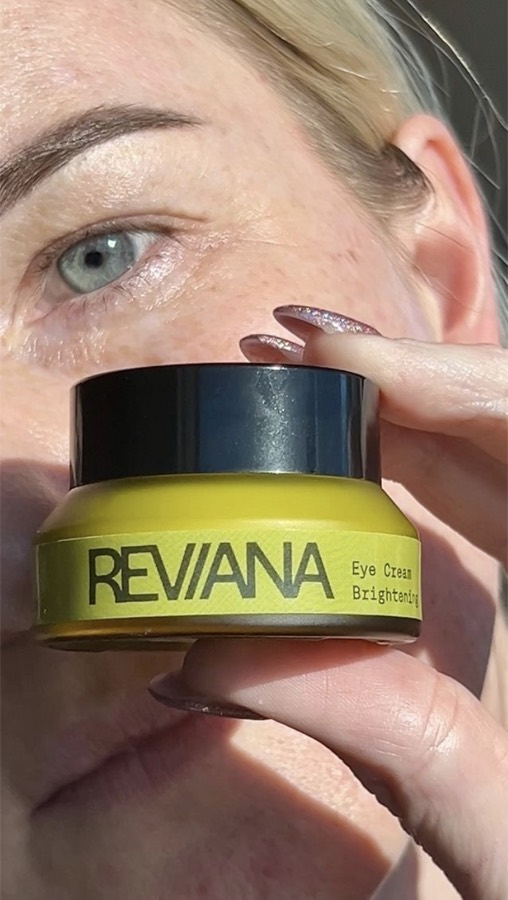 A customer holding the Reviana eye cream jar beside her eye in daylight