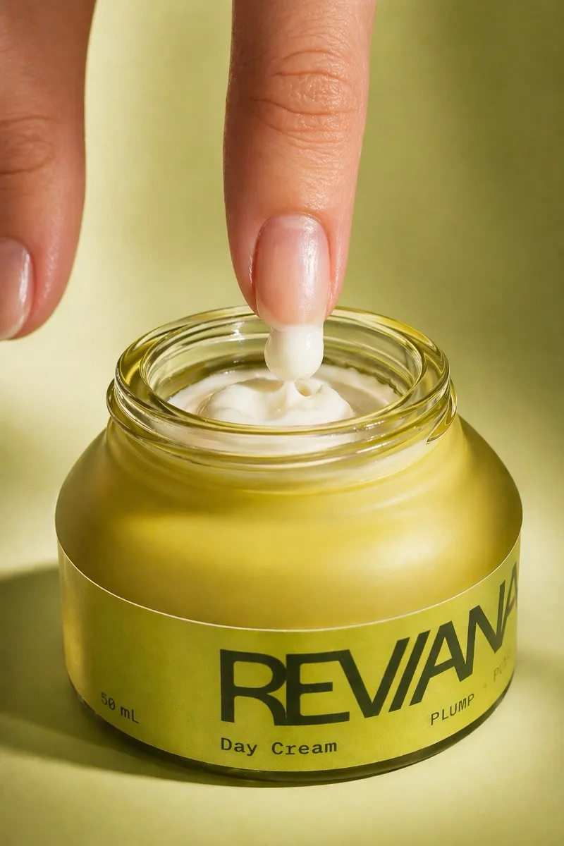 A fingertip lifting pearl-white cream from the open Reviana day cream jar